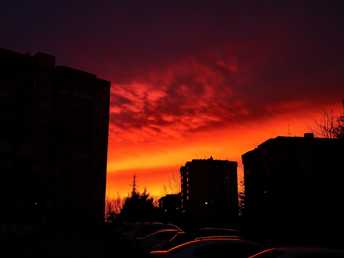 Dark apartment buildings and parked cars under a crimson pre-dawn sky in Ankara