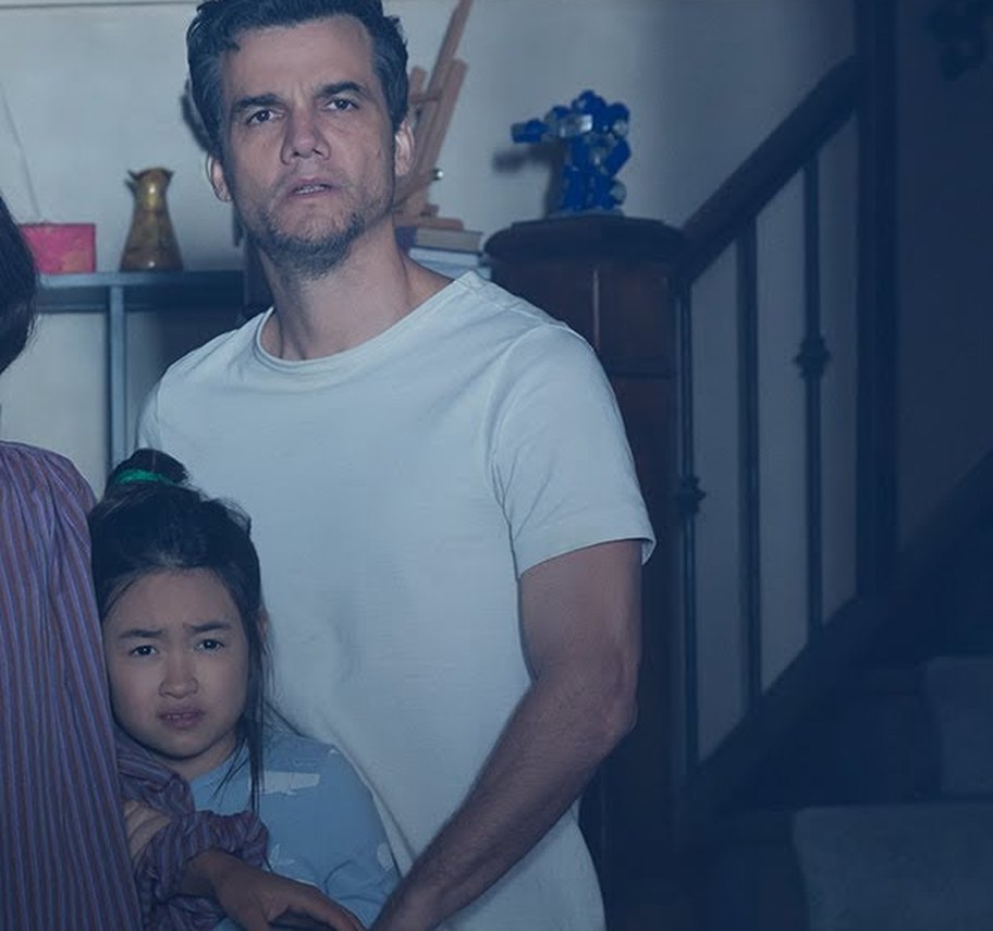A father and his young daughter standing in a dimly lit hallway near a staircase, both looking in the same direction with apprehension